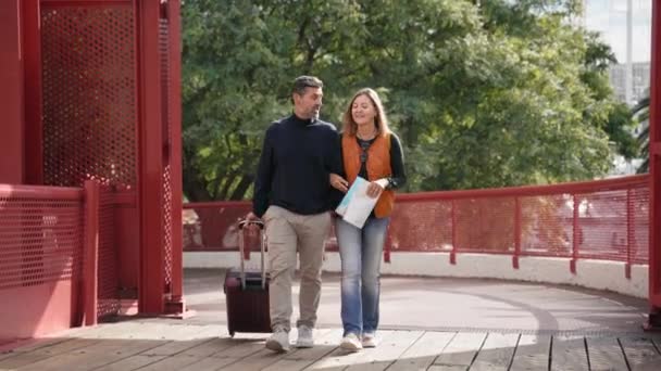 Szczęśliwa para lat 40 przybywających na wycieczkę turystyczną, spacerując z walizką udając się do hotelu na wakacje - Materiał filmowy, wideo