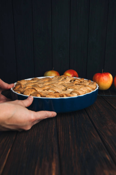 Tarte aux pommes sous forme bleue dans les mains mans sur un fond en bois foncé. Une tarte prête. Vue de face - Photo, image