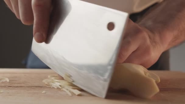 Front view of young man chef cut thin slices of a piece of ginger with knife on cutting Board. Front view of yong man cook cut thin slices of a piece of ginger. Close up of cutting a piece of ginger. - Filmagem, Vídeo
