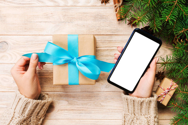 mains féminines tenir enveloppant boîte cadeau de Noël et massage de lecture sur téléphone avec ruban bleu sur table en bois brun. Vue du dessus
. - Photo, image