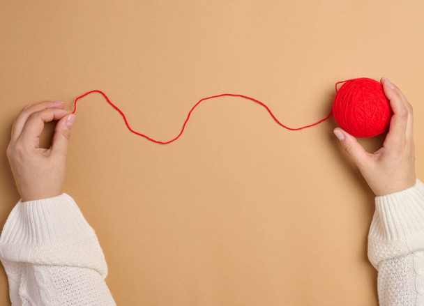 Dos manos femeninas sosteniendo una bola de hilos de lana roja para tejer, vista superior - Foto, imagen