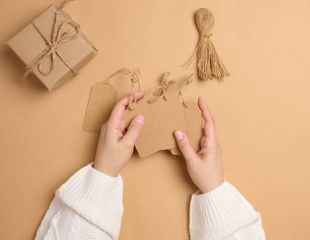 Rectangular brown paper price tags with ropes are held by female hands, top view - Photo, Image