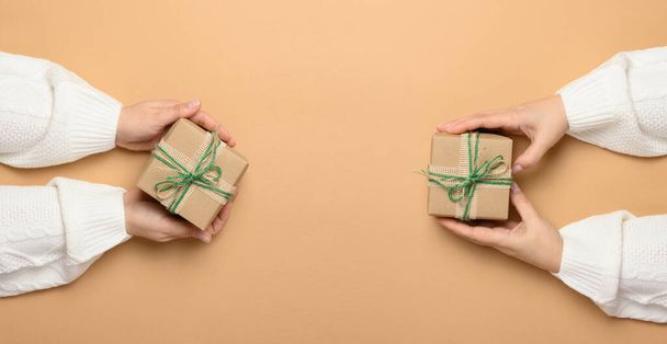 Mani femminili che tengono una scatola regalo su uno sfondo beige. Vista dall'alto - Foto, immagini