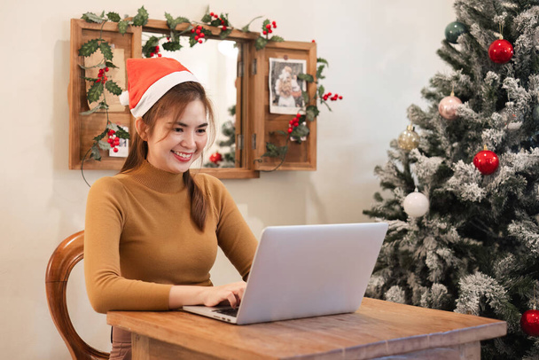 A startup employee writes a report on a laptop on Christmas Eve. In an office decorated with colorful bulbs and lights during the Christmas holidays. - Photo, Image