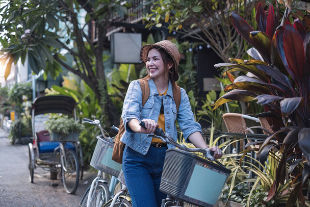 Menina turística asiática andando de bicicleta na rua de um famoso mercado local usando um belo chapéu de palha. Compras felizes no mercado local no fim de semana.. - Foto, Imagem