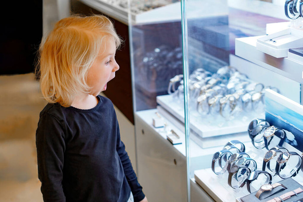 Una bambina sorpresa guarda un orologio costoso in una vetrina di un negozio. - Foto, immagini