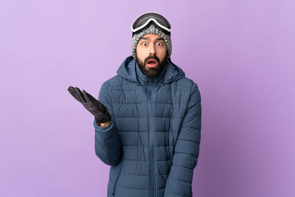 Hombre esquiador con gafas de snowboard sobre fondo púrpura aislado haciendo gestos de dudas - Foto, Imagen