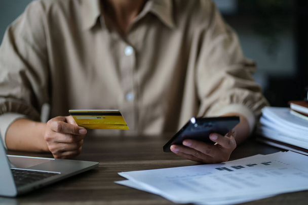 Жінка-підприємець тримає кредитну картку для покупок онлайн на смартфоні і працює над новим стартапом. - Фото, зображення