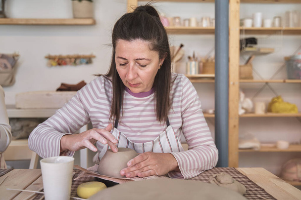 Femme avec tablier fabriquant un bol en céramique dans un atelier. Hobby et concept d'artisanat. - Photo, image