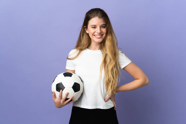 Молода блондинка-футболістка ізольована на фіолетовому фоні позує руками на стегні і посміхається - Фото, зображення