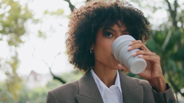 Beautiful luxurious business woman walking drinking coffee in paper cup close up. Portrait successful busy african american lady enjoy hot beverage hurrying work. Curly attractive girl going city park - Valokuva, kuva