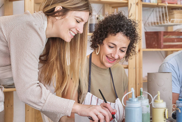 Frau lächelt, während sie einer Studentin in der Keramikklasse hilft. Hobby und Bastelkonzept. - Foto, Bild