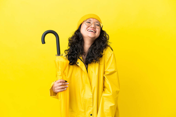 Ázsiai nő esőálló kabát és esernyő elszigetelt sárga háttér nevetés - Fotó, kép