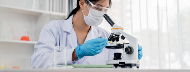 Laboratoriotutkija kehittää uutta lääkettä tai parannuskeinoa mikroskoopilla. Terveydenhuollon teknologinen kehitys tieteellisellä asiantuntemuksella laboratoriomikrobiologian laitteilla. Panoraama jäykkä - Valokuva, kuva