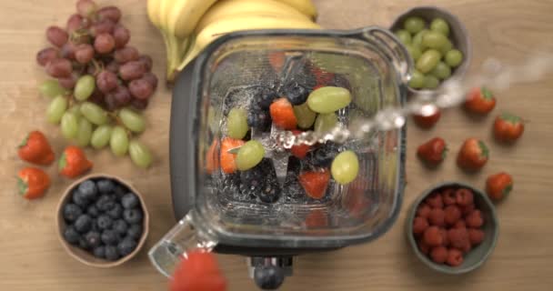 スローモーションでブレンダートップビューの視点に果物と水を注ぐ. ベリーとブドウでスムージーを作る - 映像、動画
