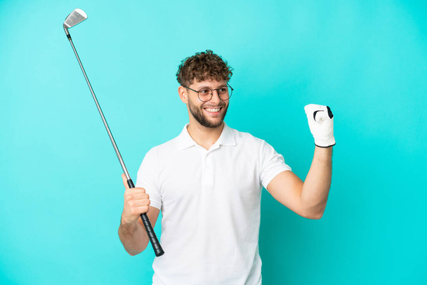 Молодой красивый белый мужчина на голубом фоне играет в гольф и празднует победу - Фото, изображение