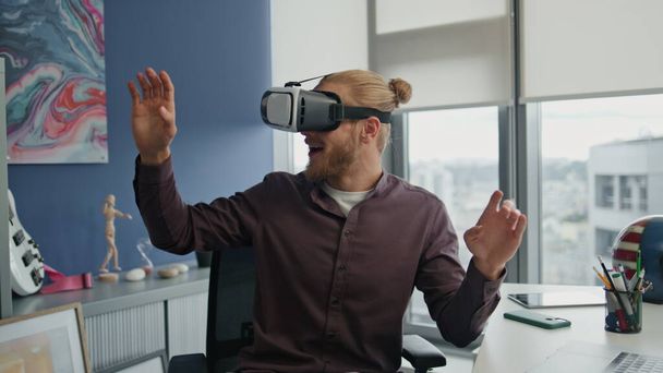 Meglepett ember élvezi a VR-t a hipszter iroda közelségében. Lenyűgöző játékos felfedezni metaverse világ távoli munkahelyen. Izgatott diák játszik új interaktív játék a modern otthon. Elképesztő fickó mozgó karokkal. - Fotó, kép