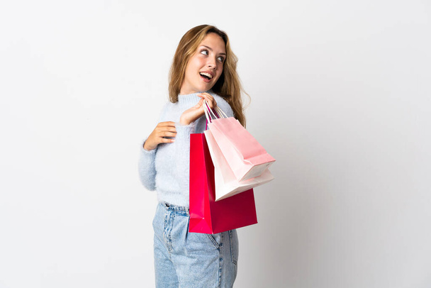 Mladá blondýna žena izolované na bílém pozadí držení nákupních tašek a s úsměvem - Fotografie, Obrázek