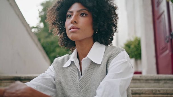Ruhige, entspannte Frau sitzt Stadttreppe Sommertag aus nächster Nähe. Attraktive nachdenkliche Afroamerikanerin in weißem Hemd, die mit der Kamera auf der Straße posiert. Schöne junge Modell entspannen im Freien. - Foto, Bild