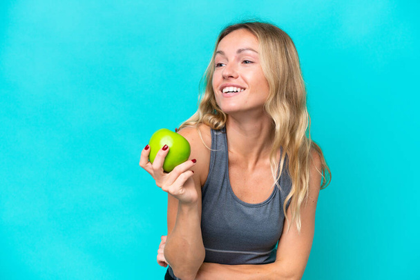 Mladá ruská žena izolované na modrém pozadí s jablkem a šťastný - Fotografie, Obrázek