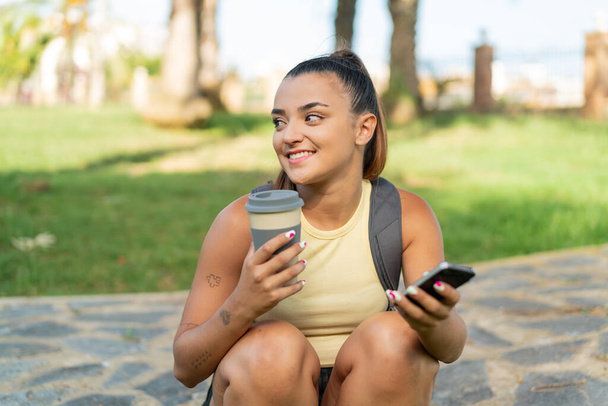 Joven mujer bonita al aire libre usando el teléfono móvil y sosteniendo un café para llevar - Foto, imagen
