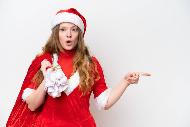 Noel elbisesi giyen, beyaz arka planda izole edilmiş, şaşırmış ve işaret eden beyaz bir kadın. - Fotoğraf, Görsel