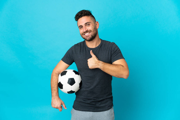 Ποδοσφαιριστής απομονώνεται σε μπλε φόντο δίνοντας αντίχειρες προς τα πάνω χειρονομία - Φωτογραφία, εικόνα