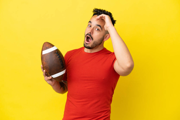 Young Caucasian man playing rugby isolated on yellow background doing surprise gesture while looking to the side - Photo, Image