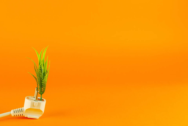  コピースペース付きのオレンジ色の背景にプラグと植物が付いたグリーンエネルギーコンセプト - 写真・画像