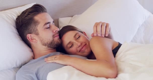 Happy, love and couple ölelés az ágyban reggel a kötődés együtt a modern lakásban. Mosoly, gondozás és fiatal férfi és nő szóló, pihenés és pihenés a hálószobában a házasság hétvégén otthon - Felvétel, videó