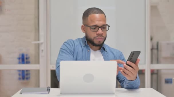 Hombre de raza mixta que trabaja en el ordenador portátil y el uso de Smartphone - Metraje, vídeo