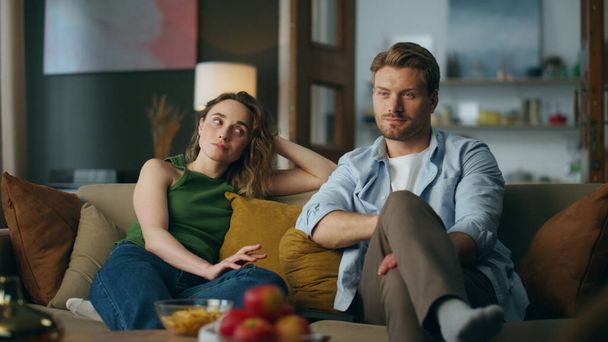 Bored spouses watching movie feeling disinterested at home. Smiling man woman looking each other started laughing at sofa. Love pair staring stupid tv show sitting at living room. Online entertainment - Photo, Image