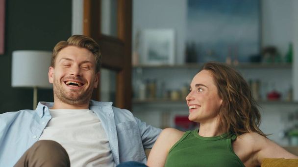 Closeup laughing couple resting sofa at home. Cheerful spouses having fun relaxing couch at modern room. Happy smiling wife husband sharing jokes together at house. Carefree pair enjoying weekend day - Photo, Image