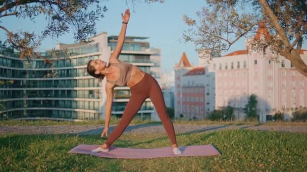 Yoga vrouw doet bochten bij zonnestralen groen park. Flexibele atleet dame stretching back warming-up spieren op groen natuur. Middelbare leeftijd sportvrouw genieten fitness routine maken driehoek asana alleen - Video