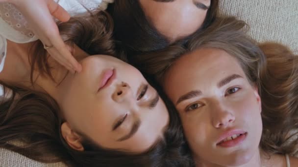 Девушки трогают идеальный вид сверху. Три привлекательные модели лежащих вместе кровать смотрит камера вертикально видео. Нежные молодые женщины наслаждаются природной красотой отдыха спа-центр. Женское сообщество. - Кадры, видео