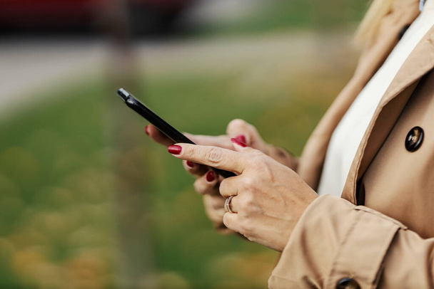 Manos de mujer sosteniendo el teléfono y mensajes de texto en una calle del centro de la ciudad. - Foto, imagen