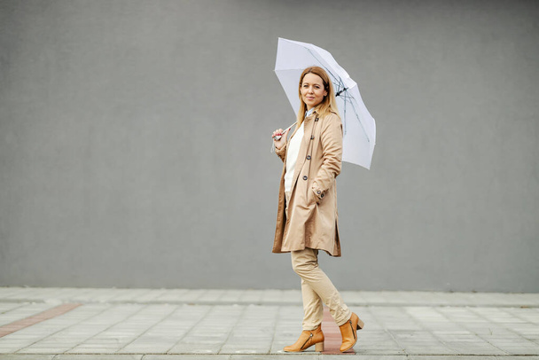 Una donna alla moda cammina per strada con l'ombrello in mano su un tempo piovoso. - Foto, immagini