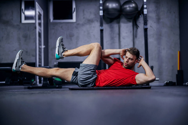 Sportsman doing bicycle lateral crunch workout at the gym. A hot male person in a fitness club doing sit-up exercises. Fitness goal, sport lover, legs extension - Photo, Image