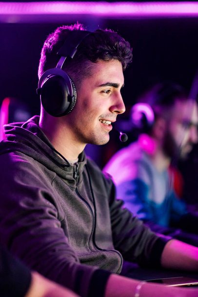 Mosolygós profi játékos headset ül a játékteremben, és videojátékok online. - Fotó, kép
