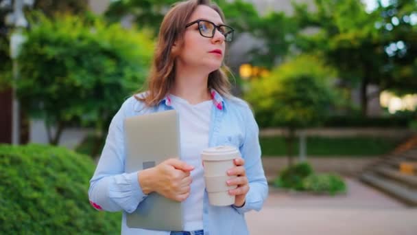Беззаботная деловая женщина, стоящая на улице с ноутбуком и кофе в руках после рабочего дня в офисе. Космический выстрел - Кадры, видео