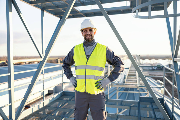 Um trabalhador está orgulhosamente em uma altura do lado de fora na construção de metal e sorri para a câmera. - Foto, Imagem
