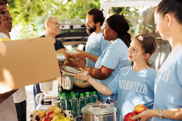 Freundliche Mädchen und Freiwillige versorgen Bedürftige bei einer karitativen Essensfahrt mit Lebensmitteln. Freiwillige verteilen Essensboxen und Spendenpakete, darunter Konserven, um Arme und Obdachlose zu unterstützen. - Foto, Bild