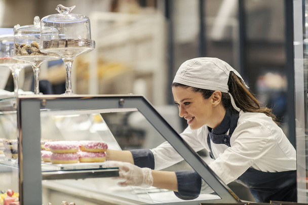 Un trabajador del departamento de panadería está vendiendo dulces en el supermercado. - Foto, imagen