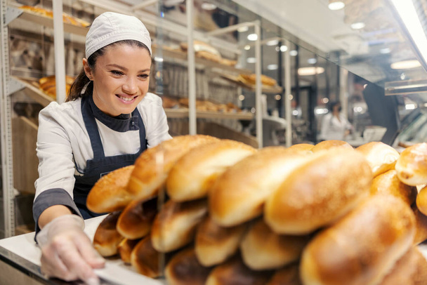 Un travailleur souriant du département de boulangerie expose des pâtisseries fraîches au supermarché. - Photo, image