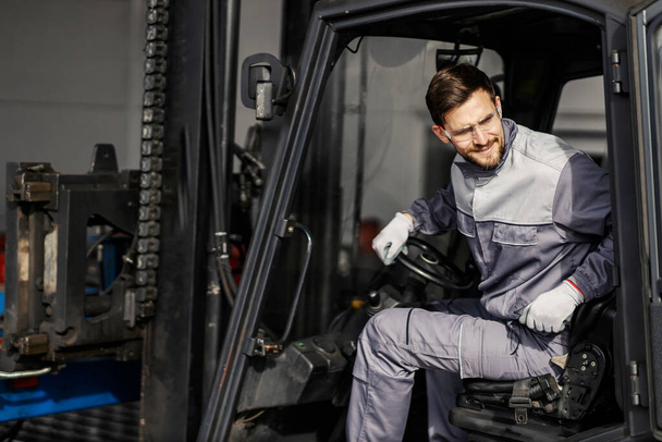 A heavy industry worker is looking over his shoulder while driving forklift. - Photo, Image