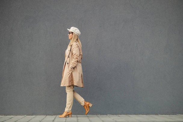 Una mujer de moda está caminando en la calle junto a una pared en el centro. - Foto, Imagen