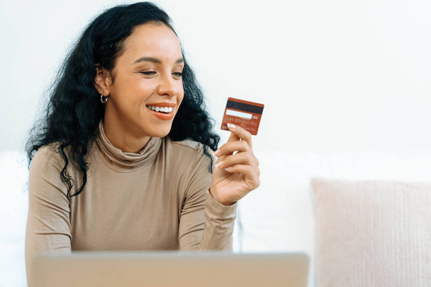 Młoda szczęśliwa kobieta kupuje produkt przez zakupy online w domu podczas zamawiania przedmiotów z Internetu za pomocą systemu płatności online kartą kredytową chronionego kluczowym cyberbezpieczeństwem z platformy sklepu internetowego - Zdjęcie, obraz