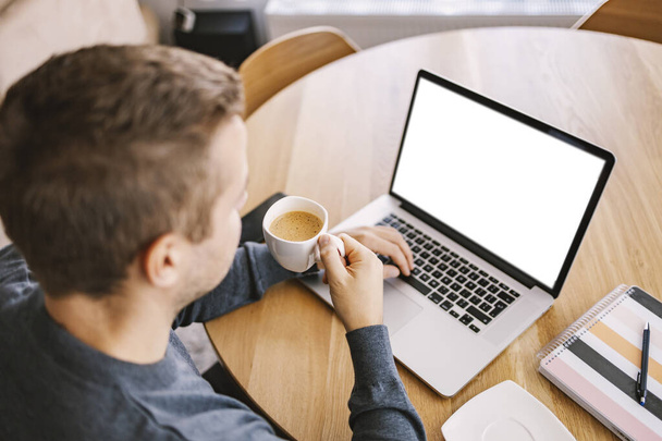 Vista posteriore di un uomo occupato beve caffè e rapporto di battitura su un computer portatile a casa. - Foto, immagini