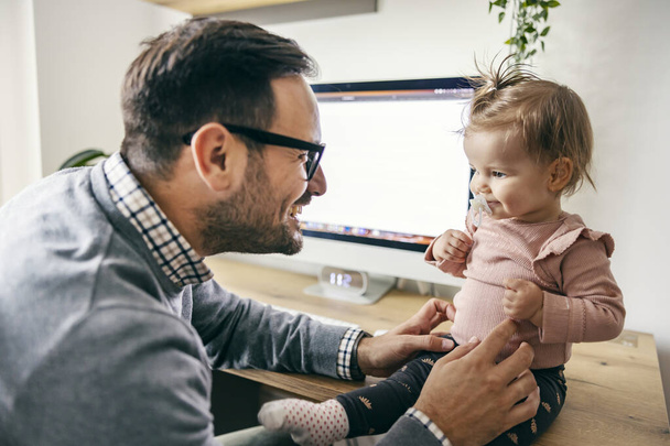 Ein Unternehmer kitzelt und spielt mit seiner kleinen Tochter in einer Arbeitspause im Home Office. - Foto, Bild