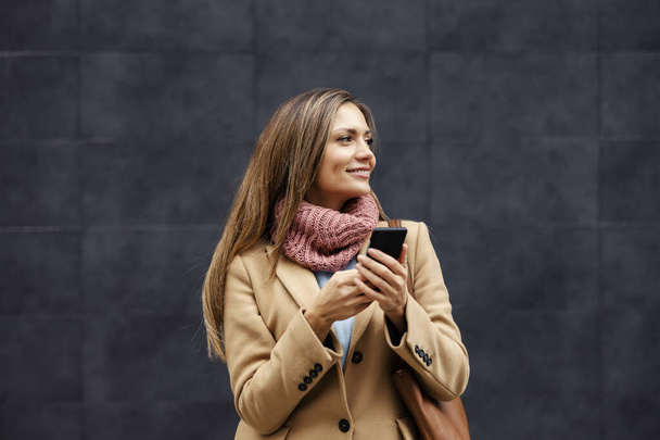 5g-Netzwerk, neue Technologien in der Telekommunikation. Eine fröhliche junge Frau in warmem Outfit steht draußen und tippt eine Nachricht auf das Smartphone. - Foto, Bild